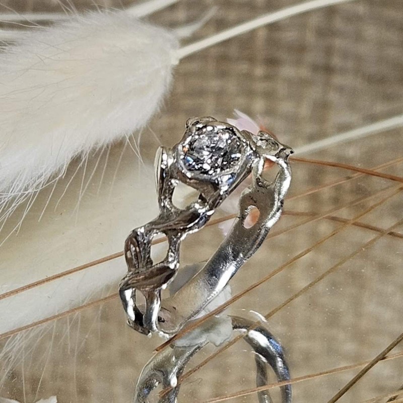 Bague aux formes entrelacées avec une pierre centrale diamant, présentée sur un miroir