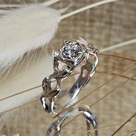 Bague aux formes entrelacées avec une pierre centrale diamant, présentée sur un miroir